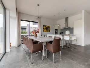 Une cuisine moderne avec des meubles blancs, un îlot central et un coin repas comprenant une grande table et des chaises.