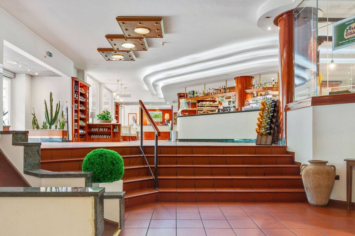 A hotel lobby with a reception desk, a staircase, and a bar area.