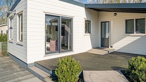Una casa moderna con patio coperto, ampie porte scorrevoli in vetro e un piccolo giardino.