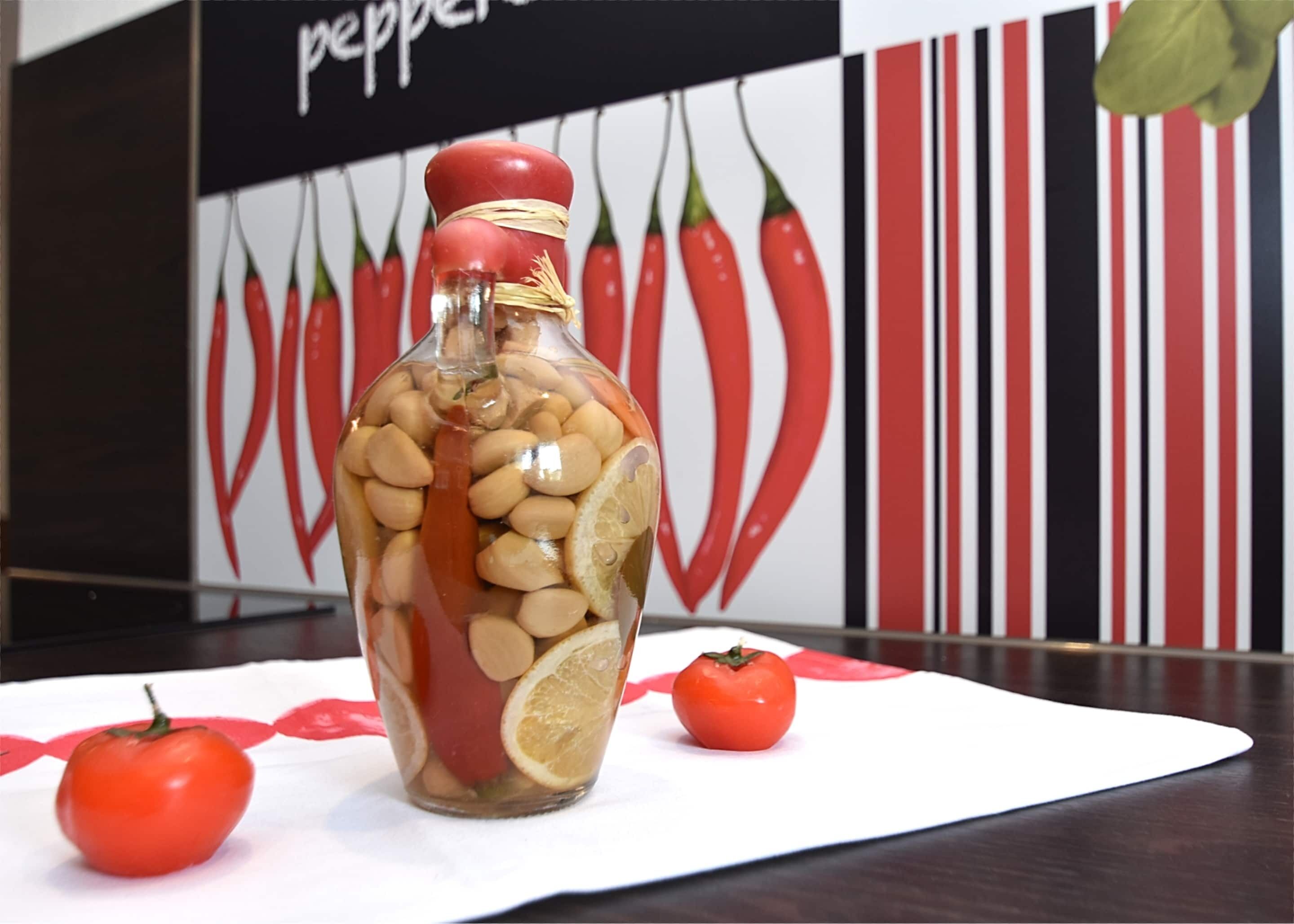 A glass jar filled with nuts and lemon slices, placed on a white cloth with two tomatoes beside it.