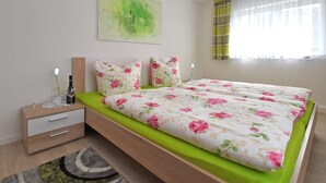 A modern bedroom with a bed, bedside tables, a nightstand, a green sofa, a wall art piece, and a window with curtains. - Cozy Apartment in Lichtenhain Germany With Garden (Sebnitz)