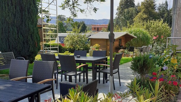 An outdoor patio with tables and chairs, surrounded by greenery and a view of the countryside. - Cozy Apartment in Lichtenhain Germany With Garden (Sebnitz)