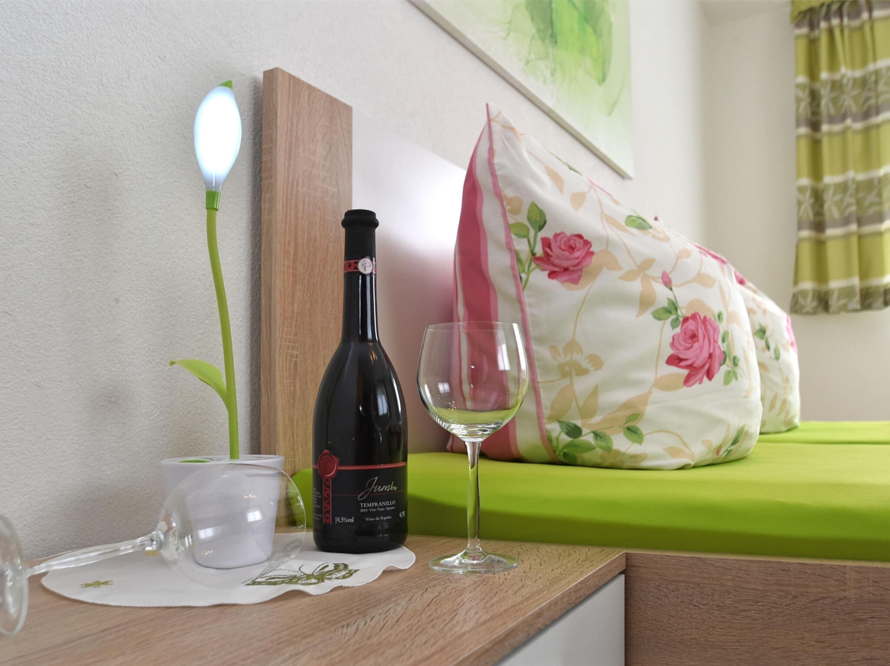 A table with a wine bottle, a glass, and a cup on a wooden surface.