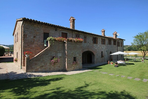 A stone building with a tiled roof, a central arched doorway, and flower boxes on the exterior wall. - Apartment on Farm Amidst the Umbrian Hills (Todi)