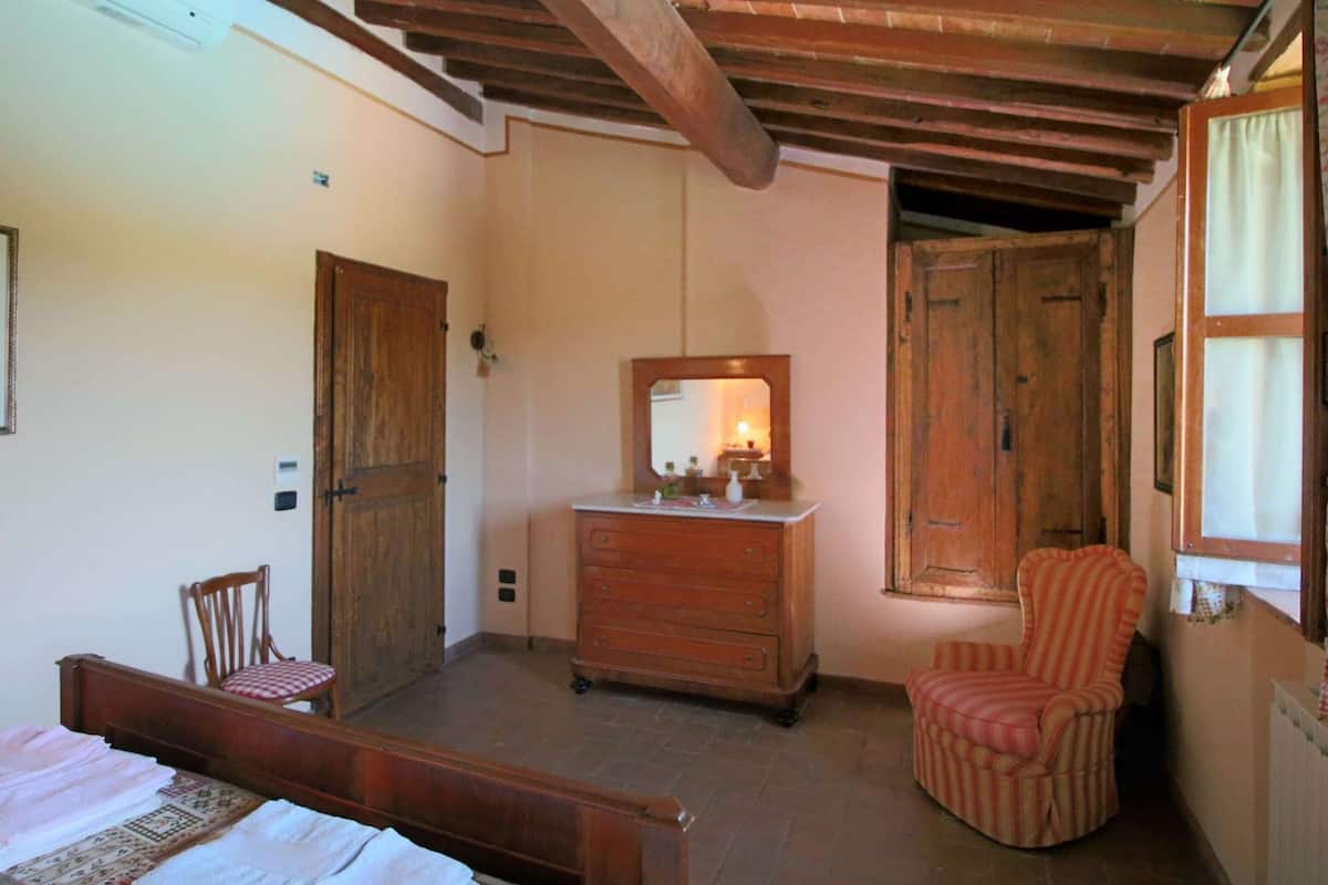 Un dormitorio con una cama de madera, un aparador con espejo, una silla y una ventana con cortinas.