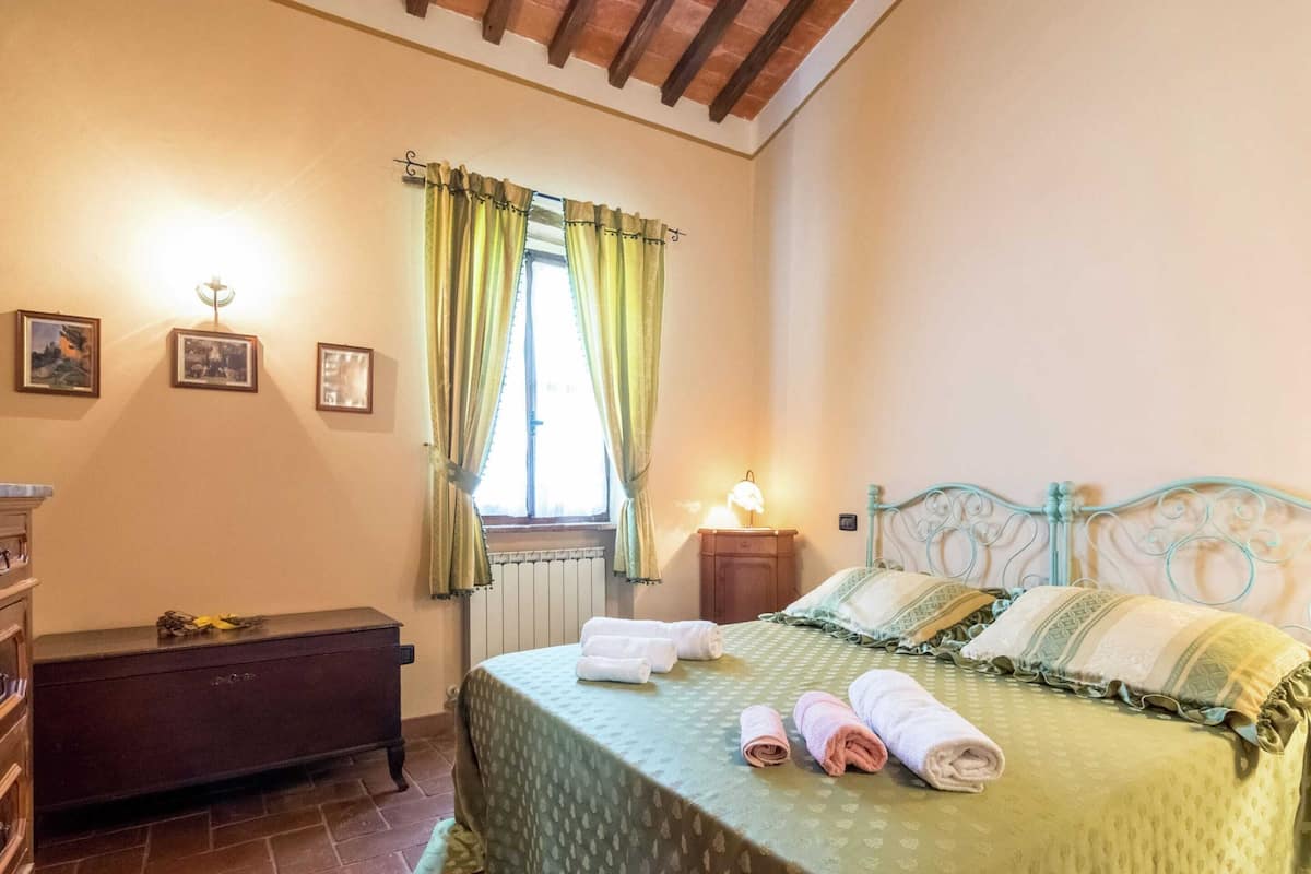 Un dormitorio con cama, cómoda, mesita de noche, lámpara y ventana con cortinas.