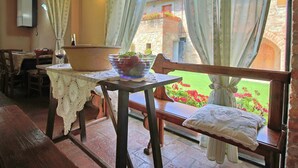 A cozy dining area with a table set for two, a large bowl of fruit, and a view of a garden through a window.