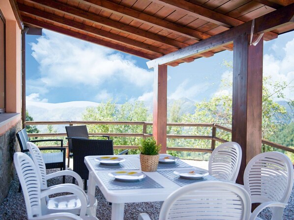 A covered outdoor seating area with a table set for two, surrounded by white chairs, overlooking a mountainous landscape. - Inviting Farmhouse in Appenines With Covered Swimming Pool (Apecchio)
