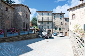 A narrow street with stone buildings, parked cars, and flower boxes along the sidewalk. - Inviting Farmhouse in Appenines With Covered Swimming Pool (Apecchio)