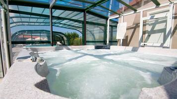 Ein Whirlpoolbereich mit Glasdach, Steinsitzgelegenheiten und Blick ins Freie.