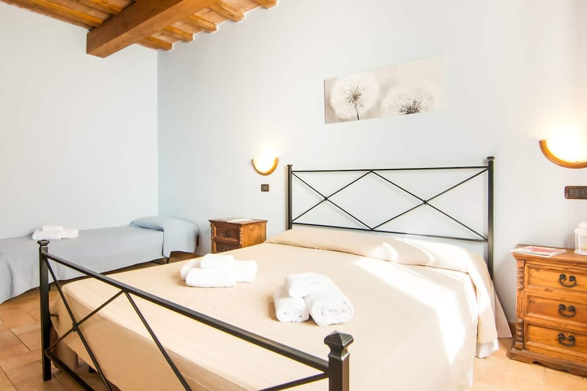 A bedroom with a bed, bedside tables, a nightstand, a wall-mounted light, and a painting.