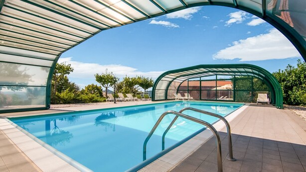 Une piscine à eau claire, protégée par une paroi de verre, entourée de chaises longues et d’une terrasse carrelée.