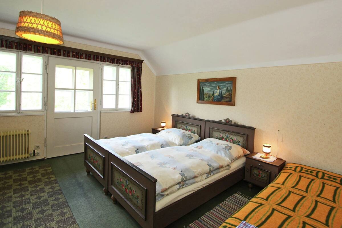 A bedroom with two beds, a radiator, a window with curtains, a painting on the wall, and a hanging lamp.