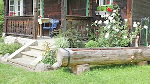 A rustic wooden house with a porch, a small table, and a chair.