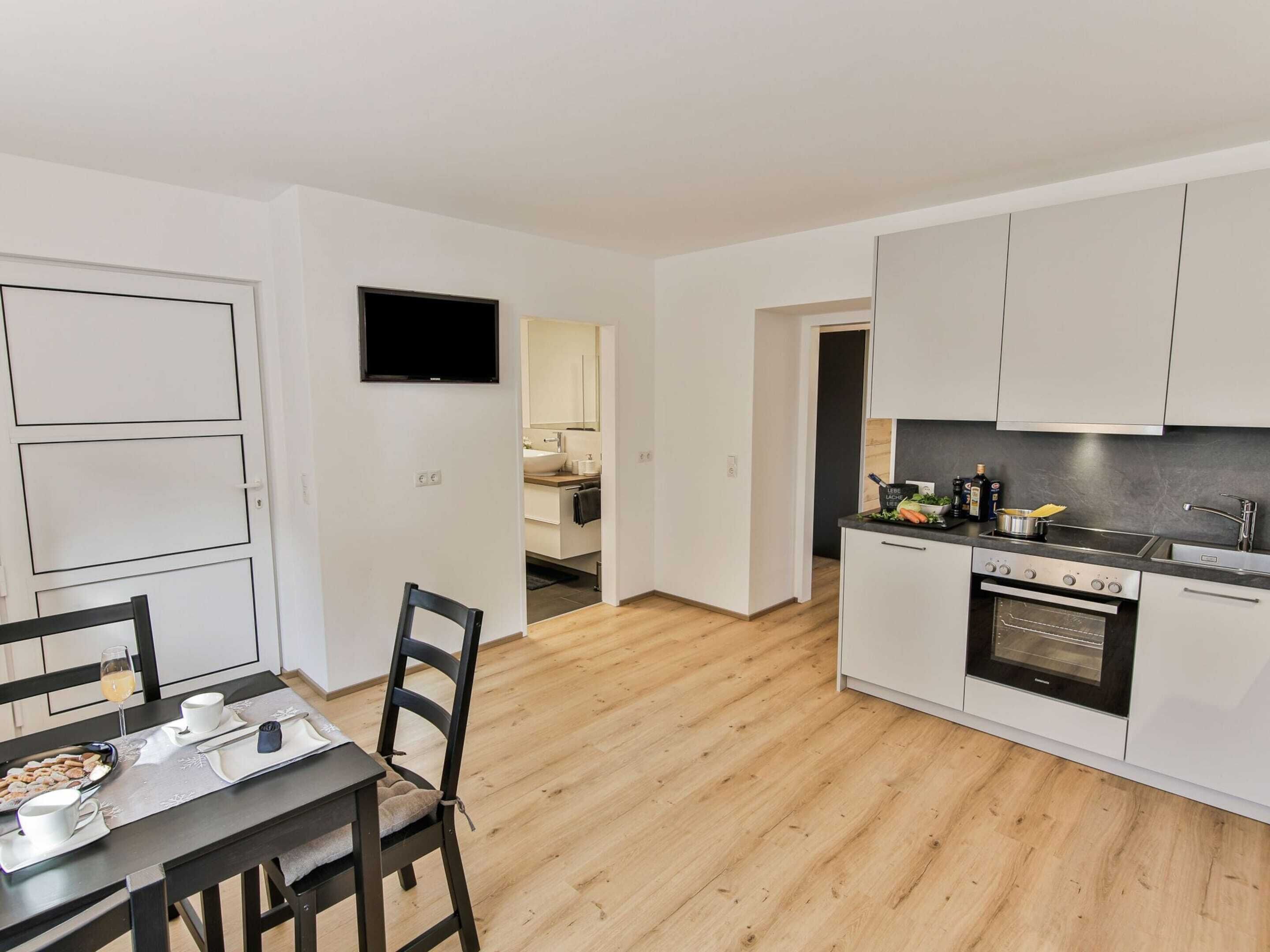 A modern kitchen with white cabinets, a built-in oven, and a dining area with a table and chairs.
