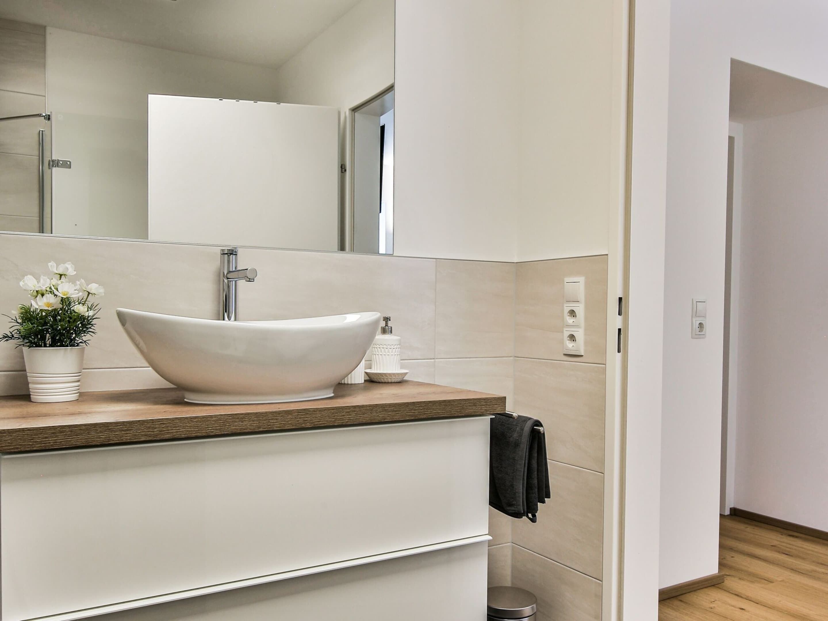 A modern bathroom with a large vessel sink, a mirror, and a potted plant.