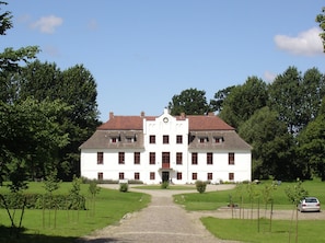 A large white building with a central entrance, surrounded by a well-maintained lawn and trees.