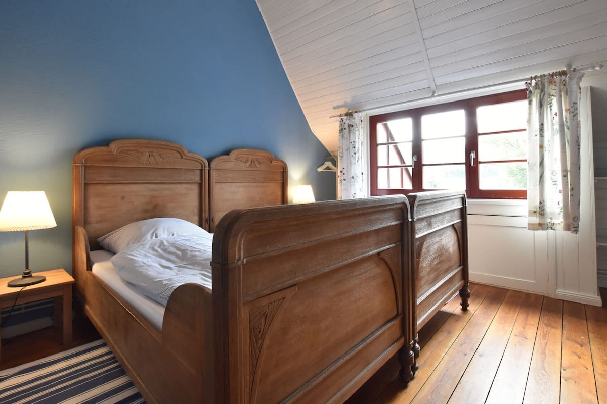 A bedroom with a wooden bed, a nightstand, a lamp, and a window with curtains.