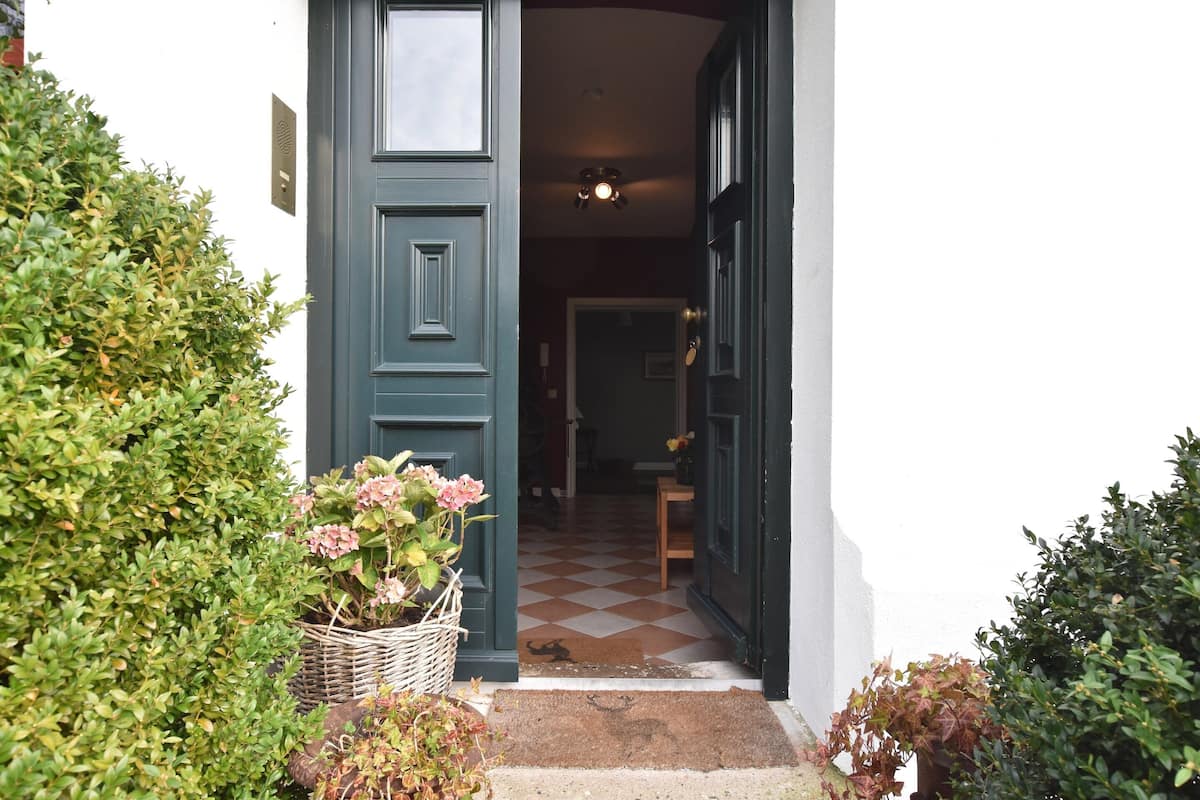 A doorway with a checkered floor leading inside, a basket with flowers, and a door with a light fixture above it.