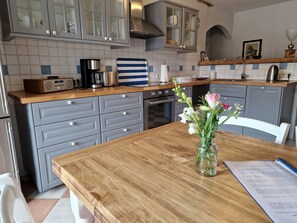 A kitchen with grey cabinets, a wooden countertop, a coffee maker, and a vase with flowers on the table. - Historic Apartment in Gerdshagen With Garden (Satow)