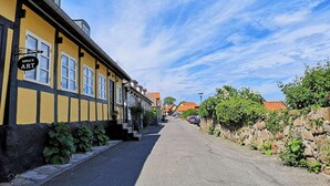 A narrow street lined with yellow buildings, one of which has a sign reading "Sosa's Art". - 6 Person Holiday Home in Allinge (Allinge)