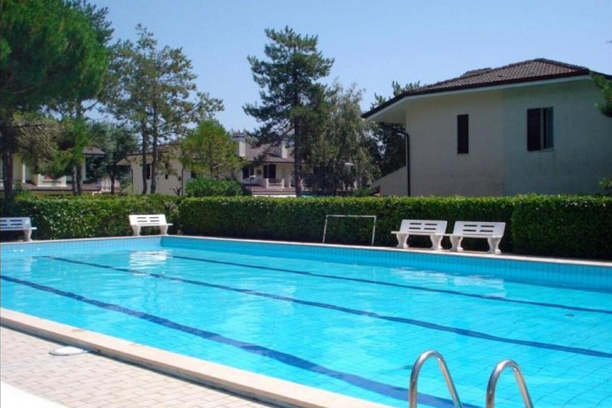 Ein Swimmingpool mit klarem, blauem Wasser, umgeben von weißen Liegestühlen und einer Hecke.