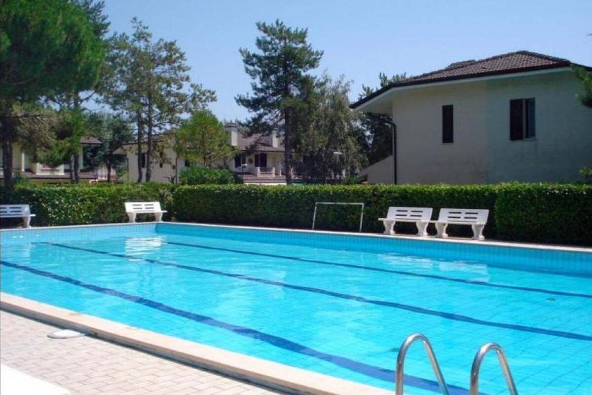 Ein Schwimmbecken mit klarem, blauem Wasser, umgeben von weißen Liegestühlen und einer Hecke.