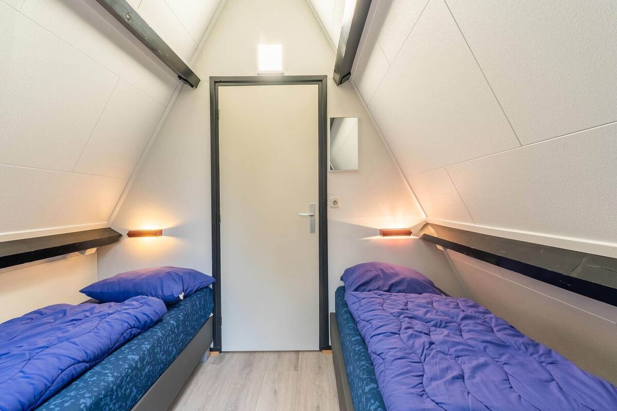 A small, triangular room with two beds, each with a blue mattress and pillows, and a door in the center.