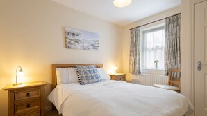 A bedroom with a large bed, two bedside tables, a nightstand, a window with curtains, and a wall-mounted picture.
