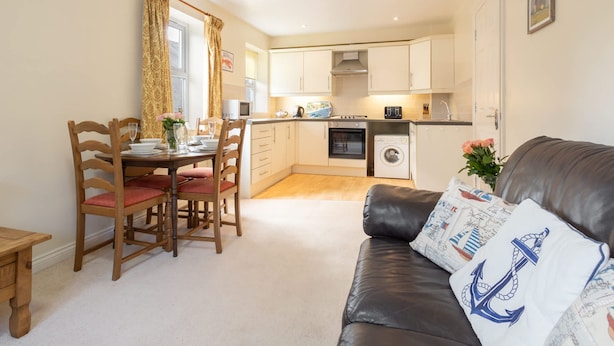 A compact living space with a dining area, kitchenette, and a leather sofa with nautical-themed pillows.