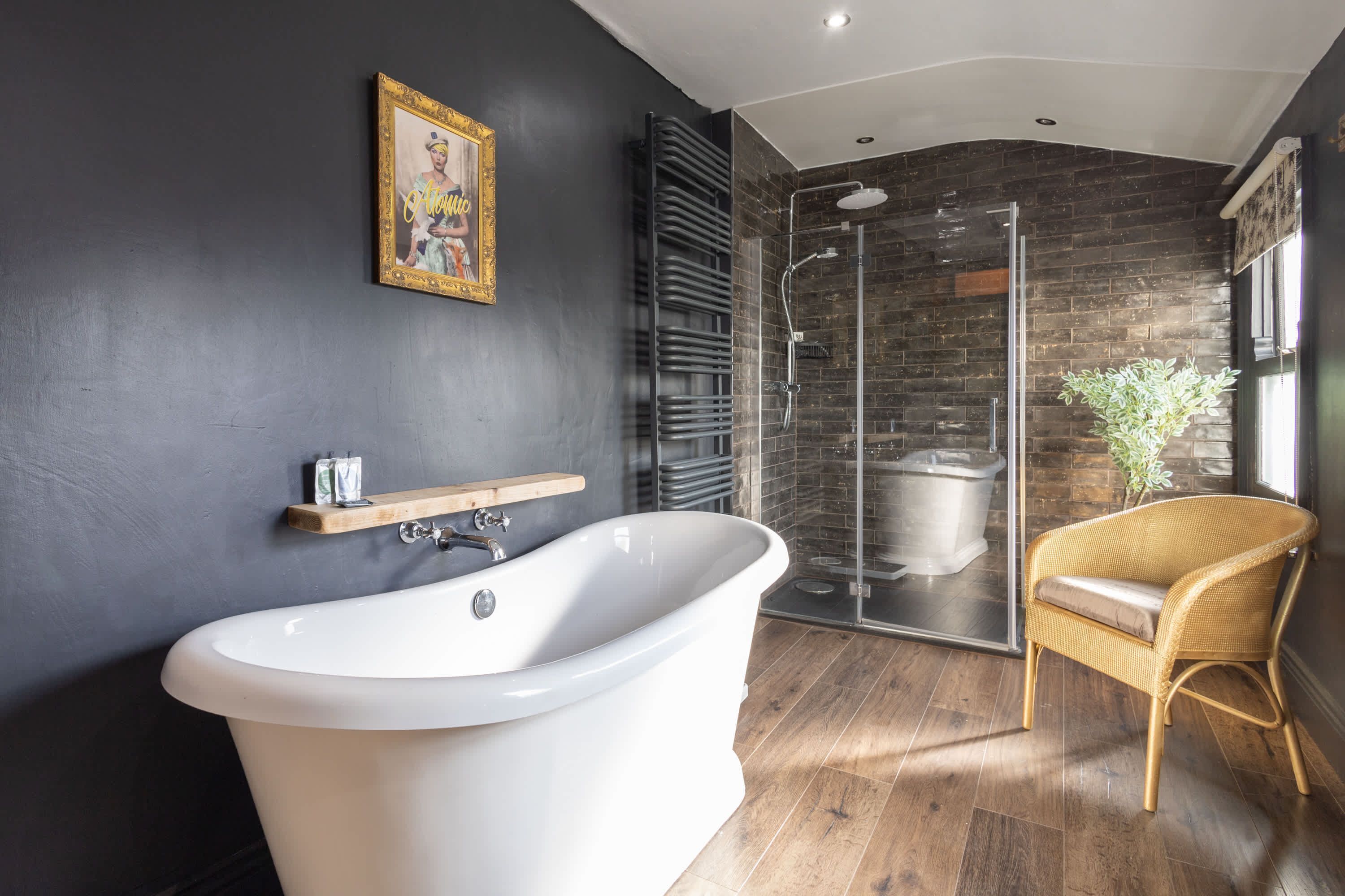 A modern bathroom with a freestanding bathtub, a glass shower enclosure, and a wicker chair.