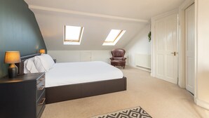 Un dormitorio con cama, mesita de noche, lámpara, silla y dos tragaluces.