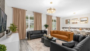 A modern living room with a black sofa, an orange sofa, a white coffee table, and a chandelier. - Upstay Championsgate Resort Home w the Best Perks (Davenport)