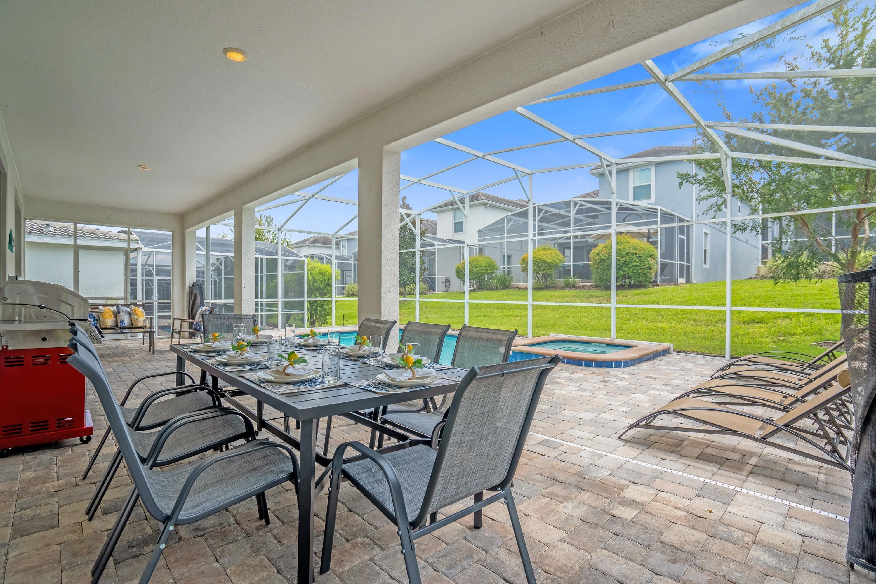A covered patio with a table set for dining, outdoor seating, and a barbecue grill.