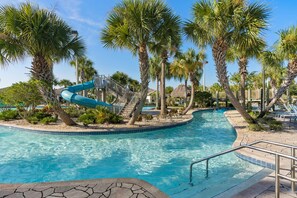 A swimming pool with a blue slide, surrounded by palm trees and lounge chairs.