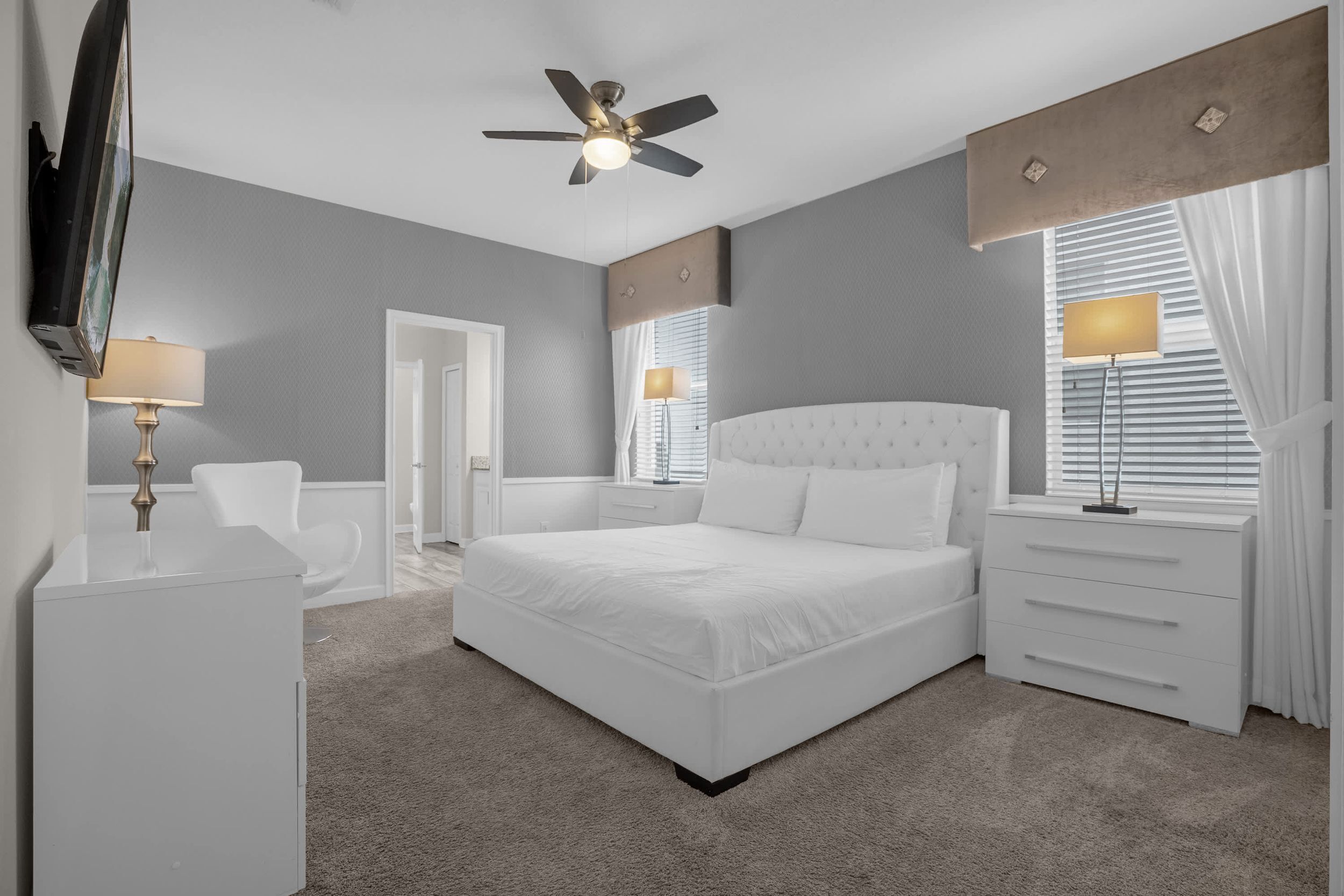 Une chambre à coucher avec un grand lit, un ventilateur de plafond, une télévision et un bureau avec une lampe.