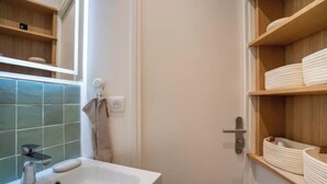 A bathroom with a white sink, a towel hanging on a hook, and shelves with folded towels.
