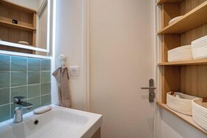A bathroom with a white sink, a towel hanging on a hook, and shelves with folded towels.