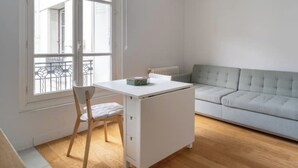 A room with a white desk, a grey sofa, and a window with a view of buildings.