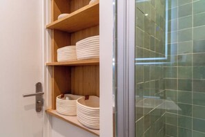 A bathroom with a glass shower enclosure and a wooden shelf with stacked plates.