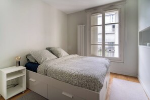 A bedroom with a bed, a nightstand, a window with a view, and a radiator.