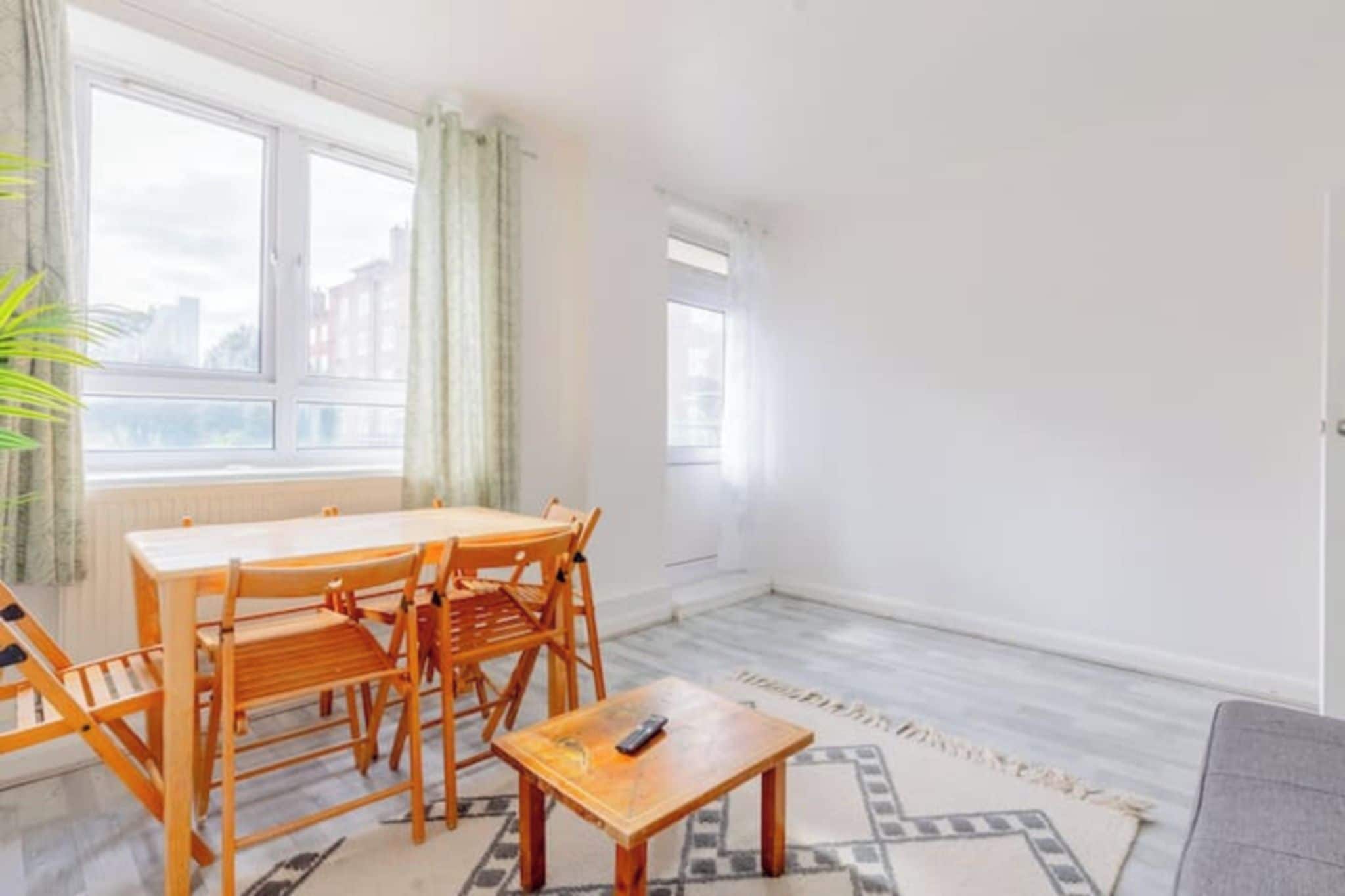 A room with a dining table and chairs, a small wooden table with a remote, and a patterned rug.