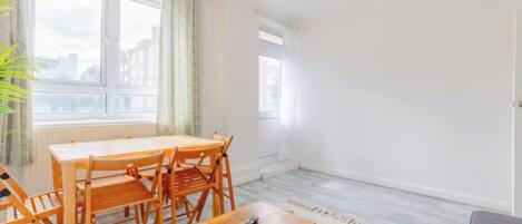A room with a dining table and chairs, a small wooden table with a remote, and a patterned rug.