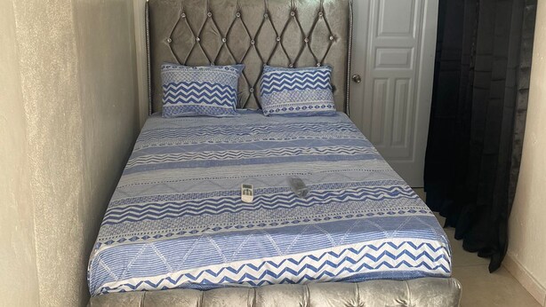 Una cama con cabecera capitonada, ropa de cama estampada y una obra de arte floral enmarcada encima.