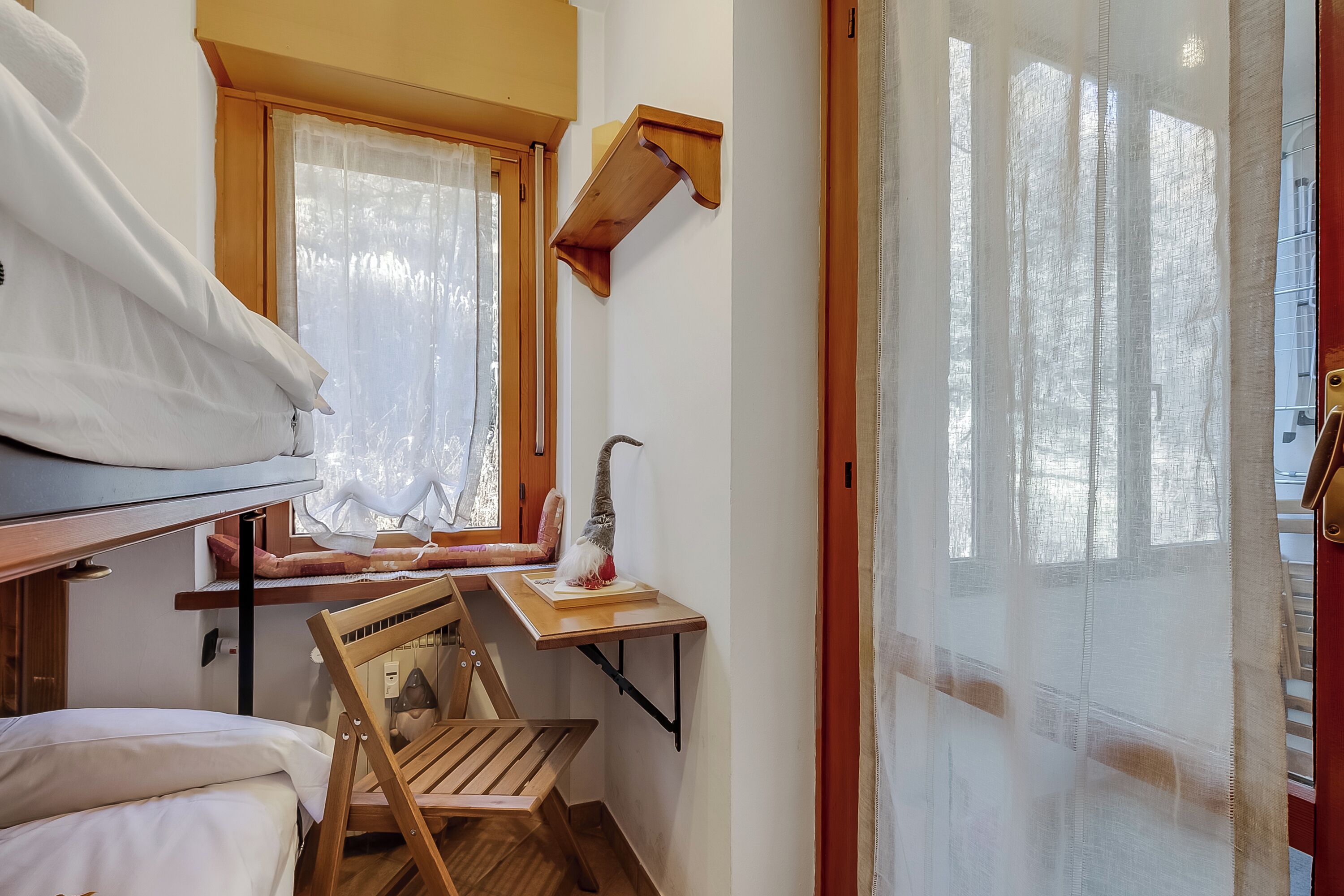 A compact room with a bunk bed, a small desk with a chair, and a window with sheer curtains.