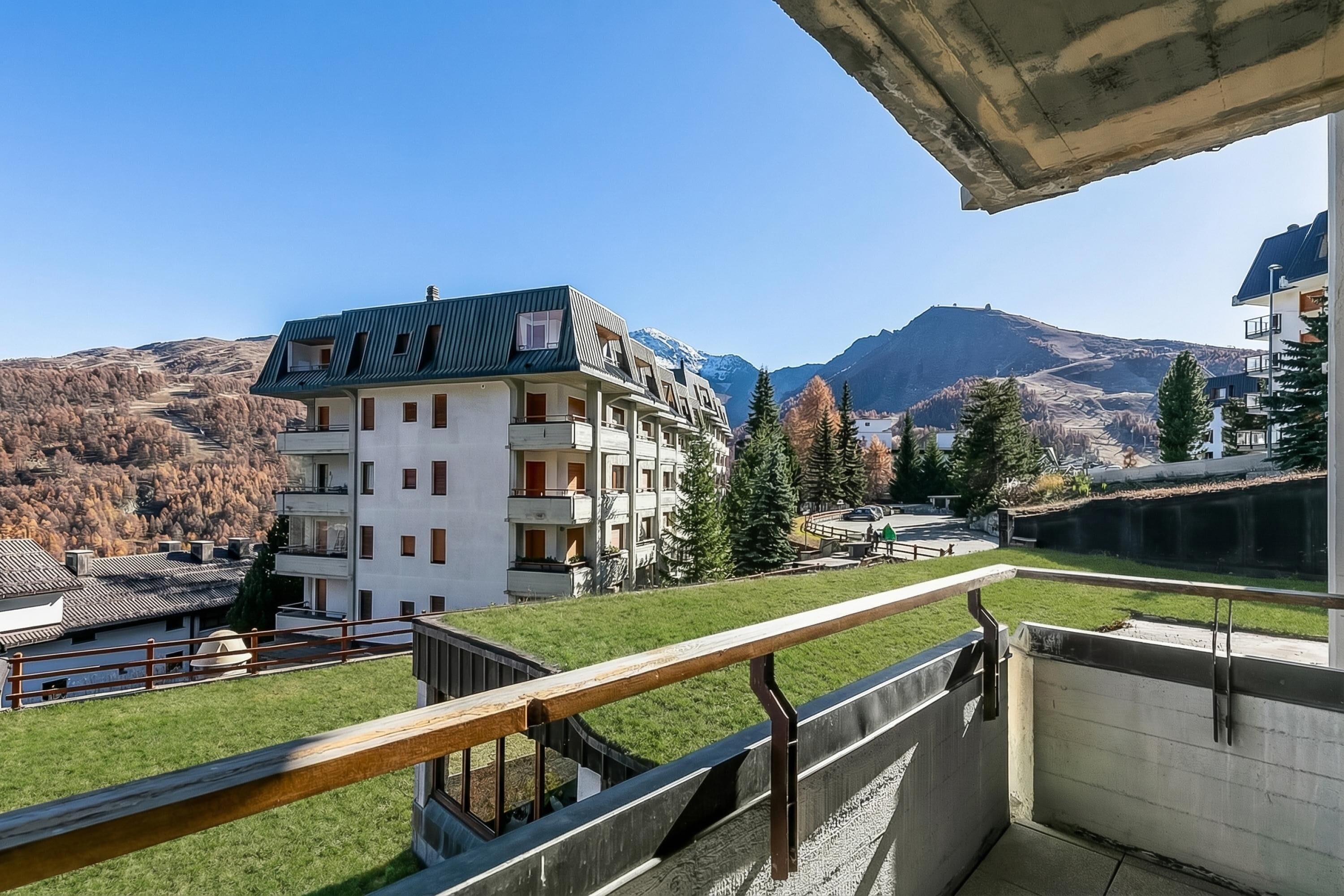 A multi-story building with balconies, a green roof, and a view of mountains.