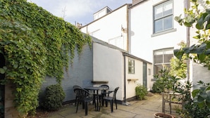 A patio with a table and chairs, a potted plant, and a white building with a window. - Host & Stay | Garnet Street (Saltburn-by-the-Sea)