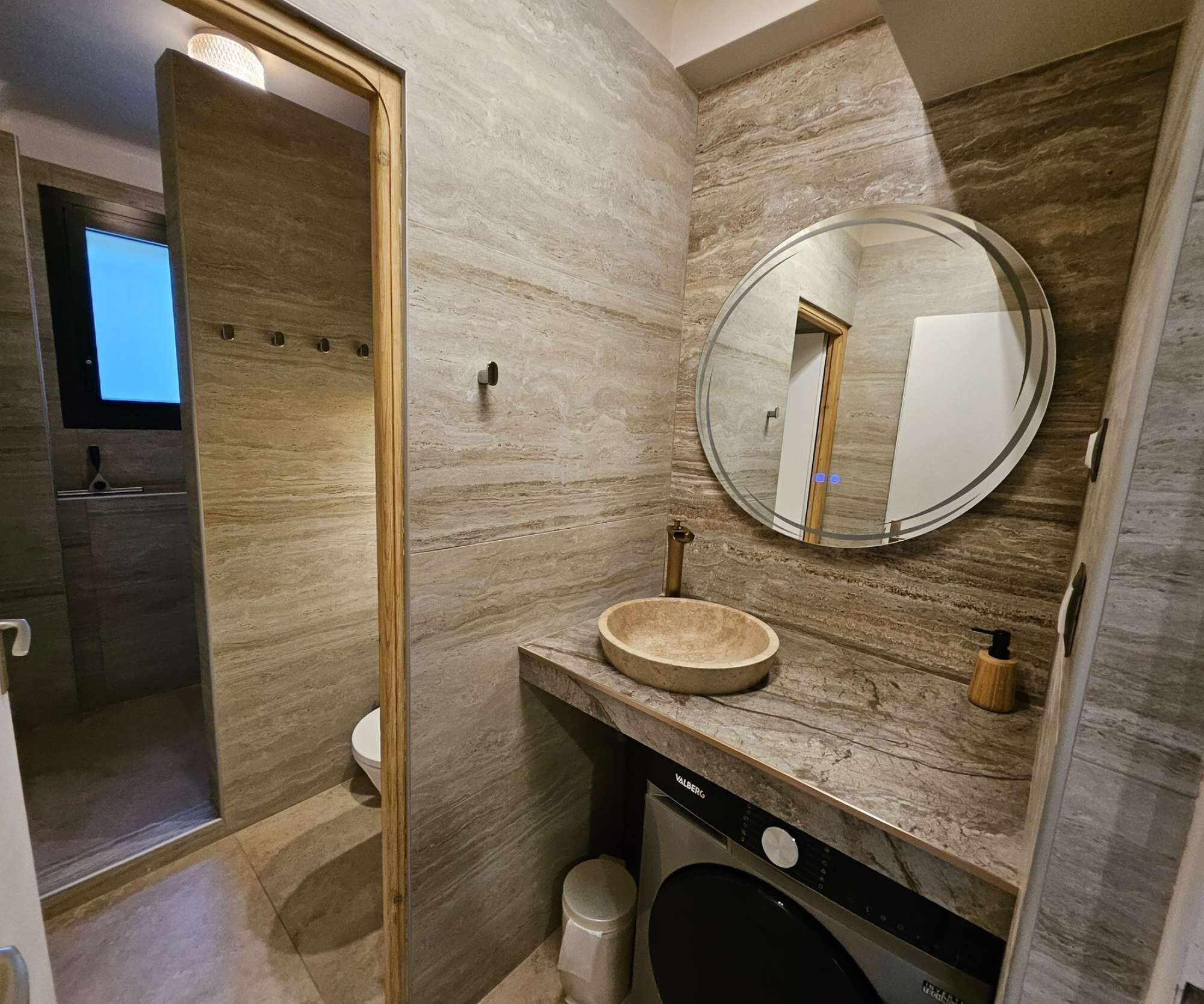 Ein modernes Badezimmer mit Marmorwand, rundem Spiegel, Waschbecken und Toilette.