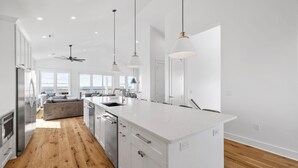A modern kitchen with white cabinetry, a large island, and pendant lighting. - Gulf Views w/ Pool, Firepit and Games (Port St. Joe)