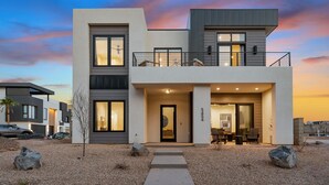 Ein modernes, zweistöckiges Haus mit Balkon, Auffahrt und einem gepflegten Garten.